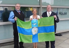 Charles Ashburner (Flag Institute Chief Executive), Helen Edwards (DCLG Director General), and Graham Bartram (Chief Vexillologist, Flag Institute) hold the North Riding flag.